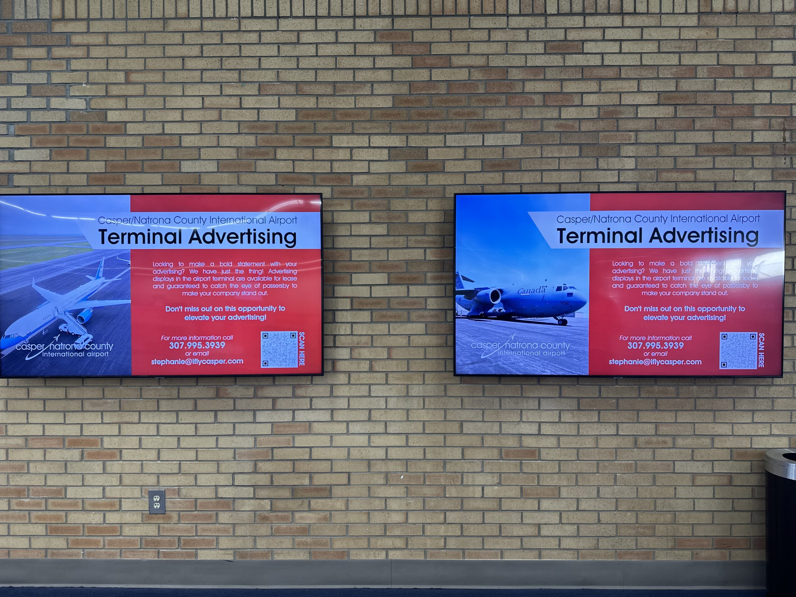 Digital advertising monitor mounted on a terminal wall in a high-traffic area of the airport