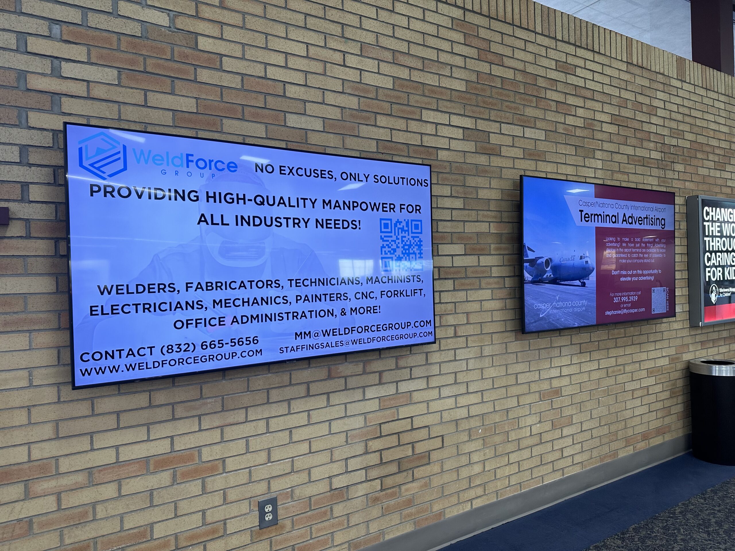 Digital advertising monitor mounted on a terminal wall, displaying a paid advertisement